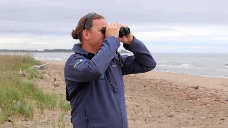 A man looks through binoculars on a beach. 