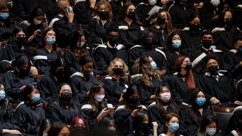 Dozens of students wearing regalia and face masks attend their convocation at the University of Toronto.