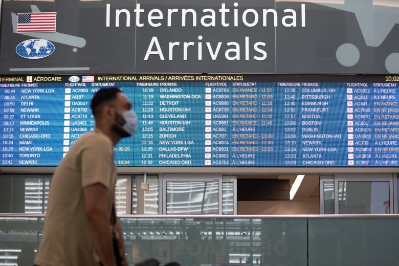 A man walks by the arrivals board in an airport.