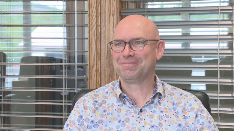 A smiling bald man wearing glasses and a colourful shirt.