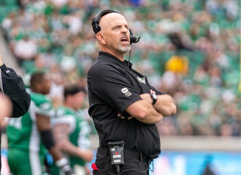 Football coach watches game on sideline with arms crossed