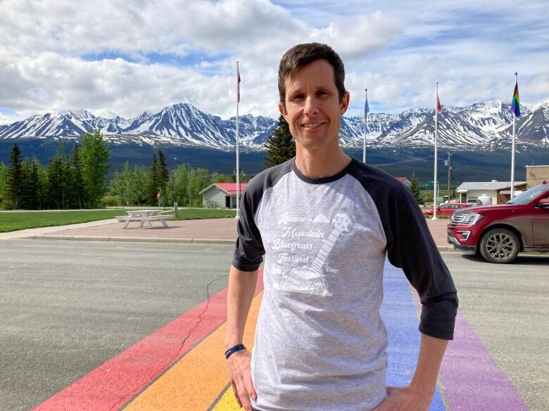 A man stands on a street with mountains in the background.