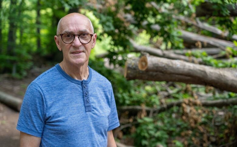 A man stands in front of a pile of downed trees.