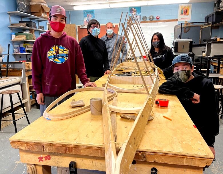 Four junior high students, their instructor and their principal pose near the wooden frame of a kayak that is being assembled. 