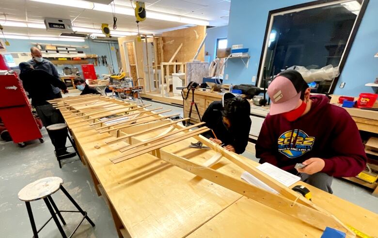 Two boys focus on their work of building a kayak, which is attached to a frame. 