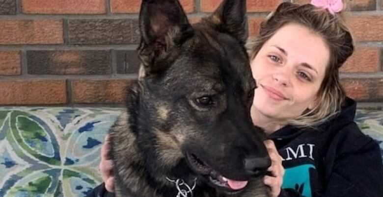 A woman in a pink ponytail holds a young black dog.