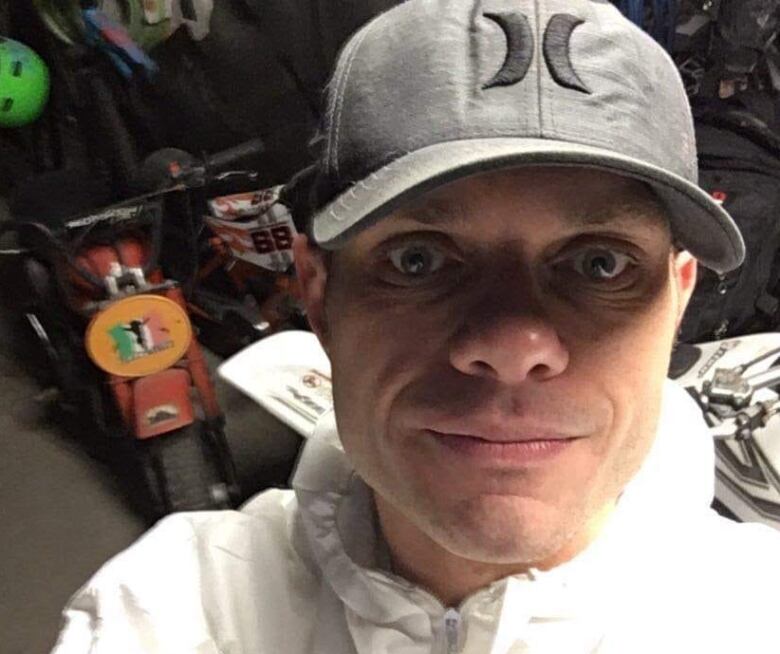 A man wearing a white hat and white jacket standing inside a garage. 