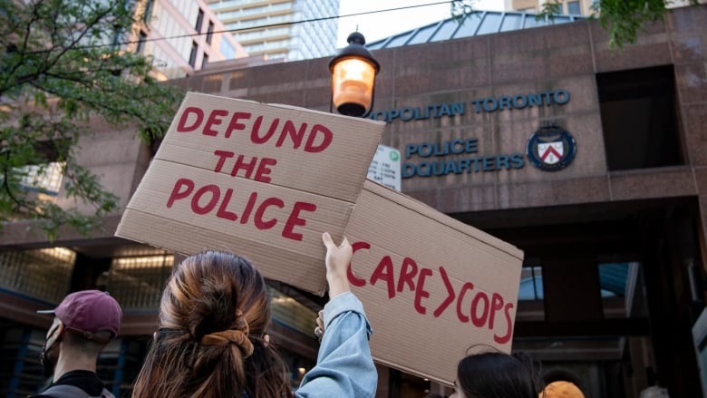 Protestors hold up signs saying defund the police outside Toronto police headquarters