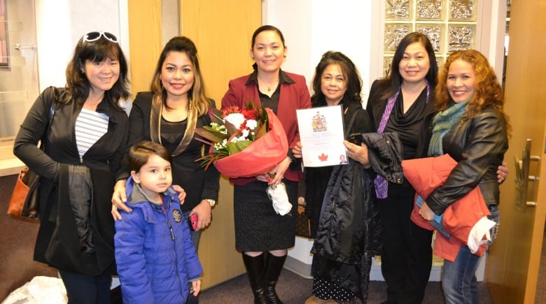 A group of Filipino women smile and pose for a photograph. One woman holds a bouquet of flowers.