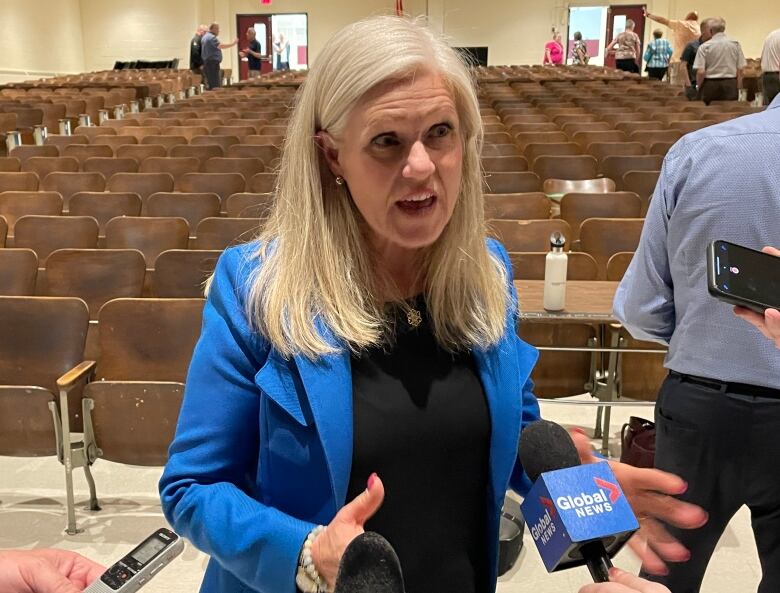 Moncton Mayor Dawn Arnold shown with reporter microphones around her in an auditorium. 