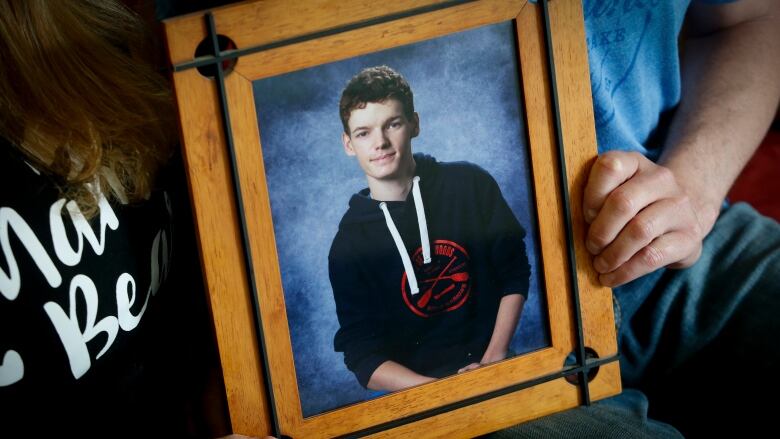 Two people hold a framed photo of a teenaged boy.