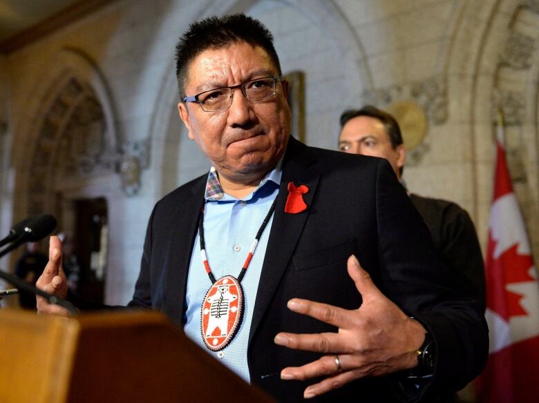 A man gestures with his hands as he speaks at a podium.