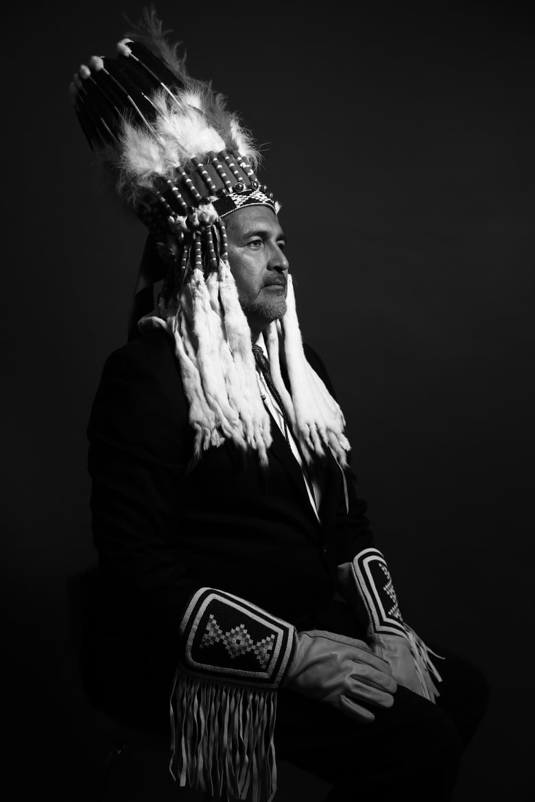 A black-and-white photo of the side profile of an Indigenous man in traditional attire