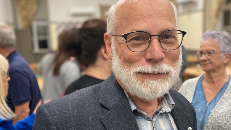 A man smiles wearing glasses and a suit jacket.