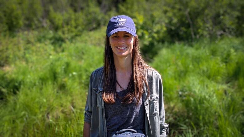 Young woman wearing baseball cap smiling in a grassy area.