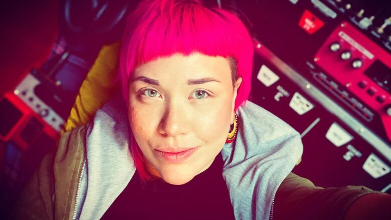 A woman with pink hair looks into the camera as she takes a selfie.