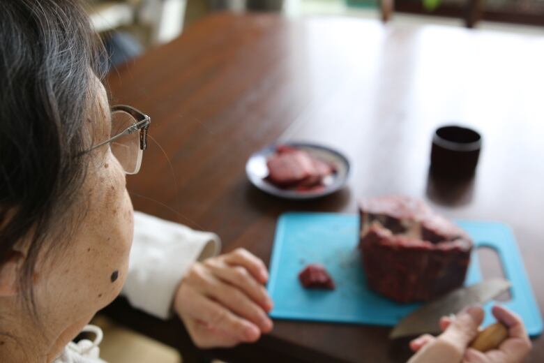 woman with ulu cuts frozen caribou meat