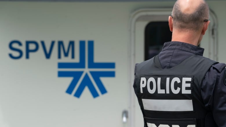 A police officer is seen from the back. In the background, a mobile unit sports the SPVM logo.