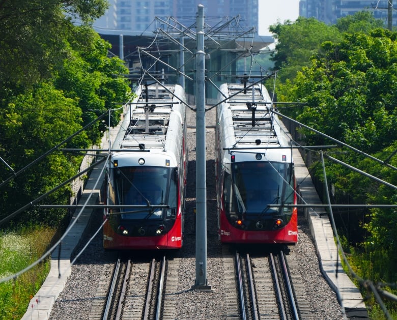 Two red and white light rail trains next to each other on the tracks.