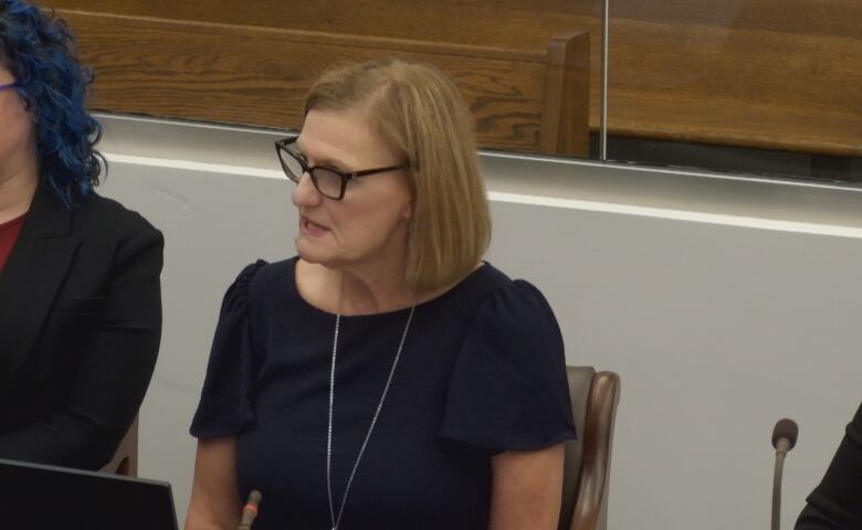 A woman sits in a chair, speaking.