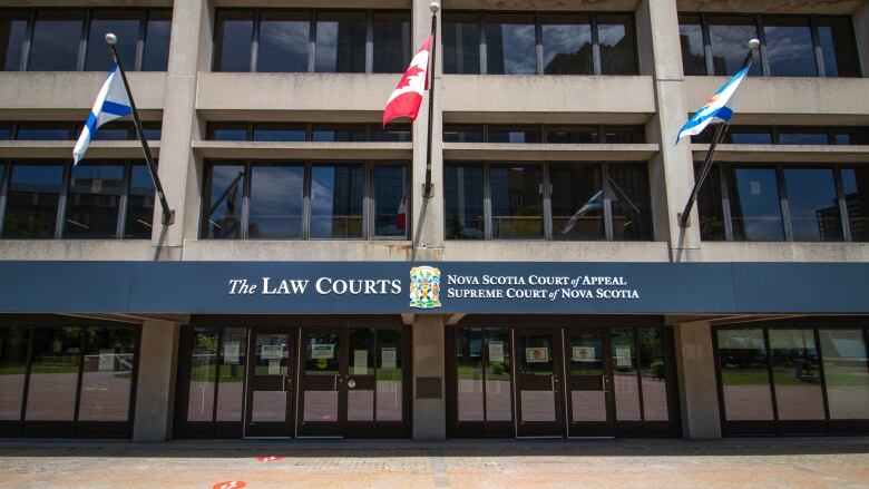 A Canadian flag and two others flutter outside of an austere court building. 