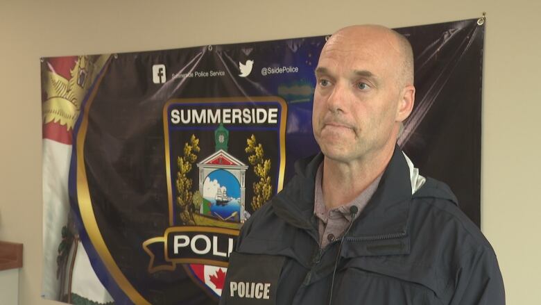 Police officer standing in front of a banner, looking off-camera. 