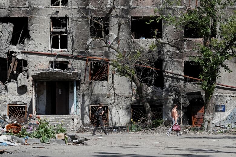 People walk past a heavily damaged residential building.