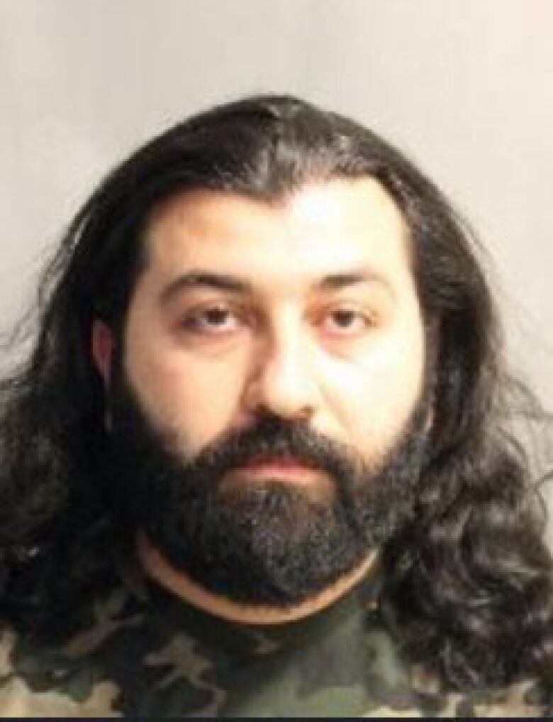 A police mug shot of a man with black hair and a beard.