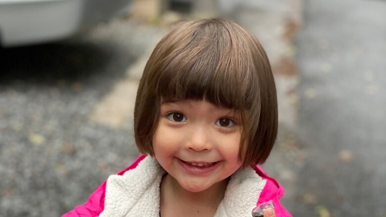 A little girl wearing a bright pink coat smiles and holds up a small rock.