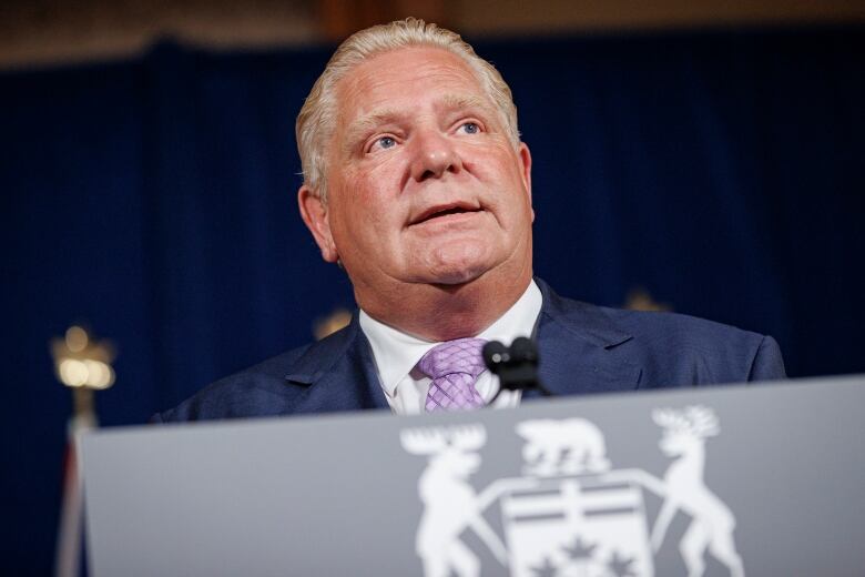 A man in a suit speaks at a lectern.