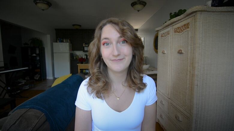 Tiffany Wice, a white woman in her 20s faces the camera, she has wavy dark blonde hair, a white top and pink eyeshadow. 