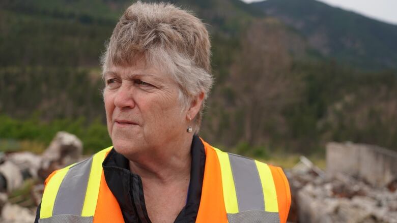 A woman in a high visibility vest looks to the left as the wind blows through her short greying hair.