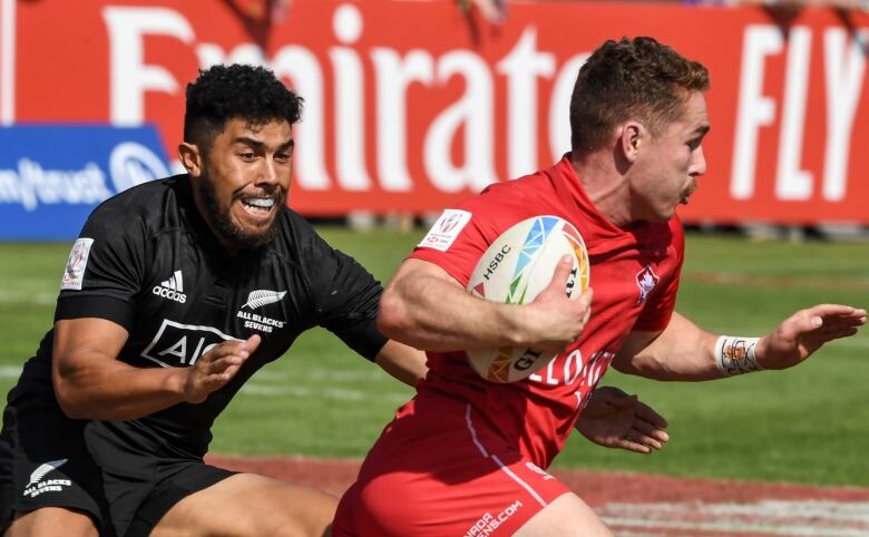 A rugby player from New Zealand wearing a black jersey vies for the ball against Canadian Cooper Coats, who is wearing a red shirt, in a Dec. 6, 2019, match.