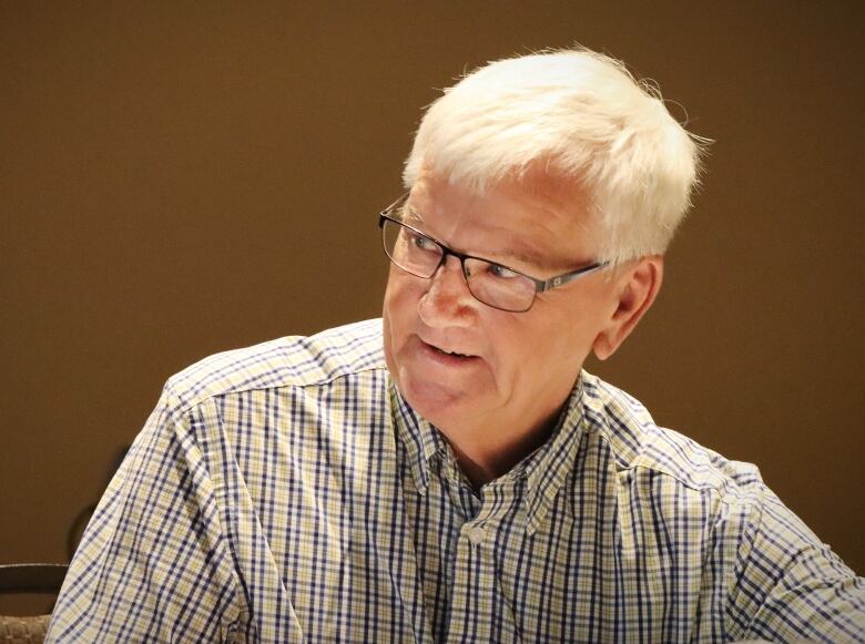 A man with white hair, glasses and a plaid shirt smiles.