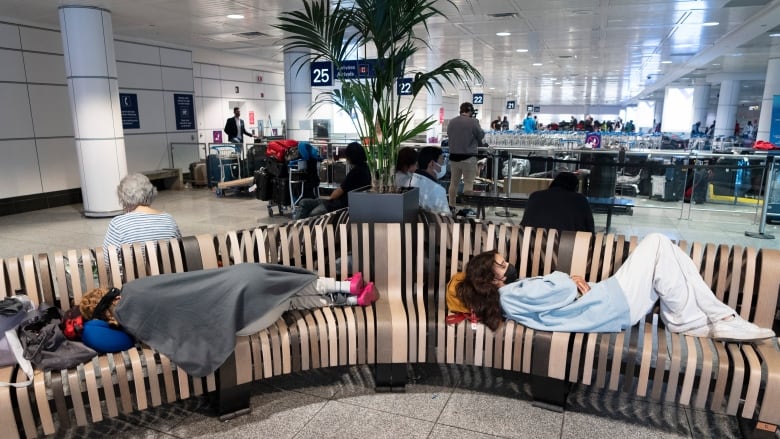 People sleeping on benches in an airport.