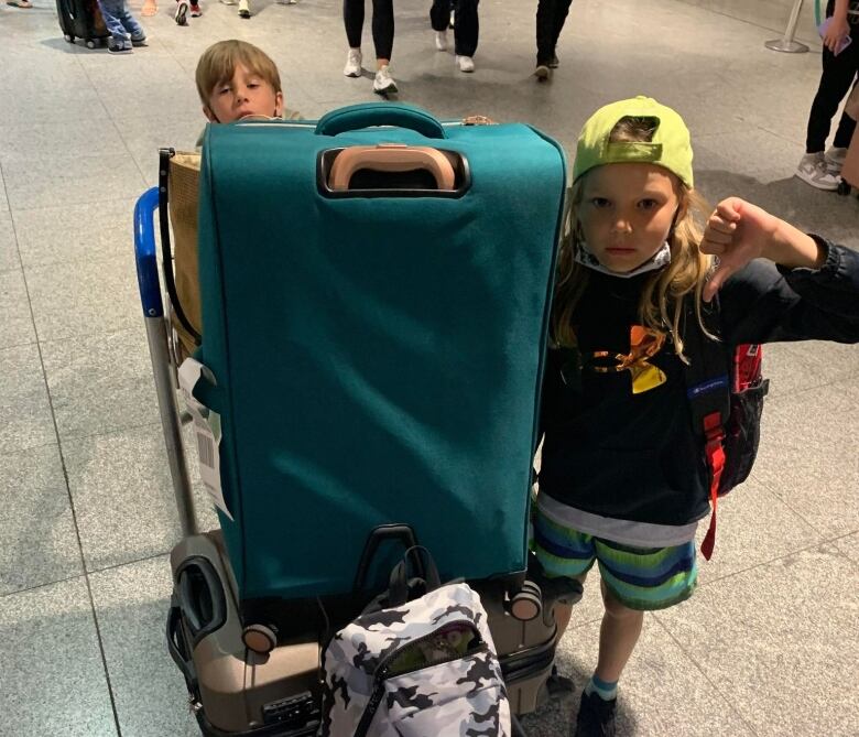 A girl gives the thumb down side as she stands beside a large suitcase and her brother.