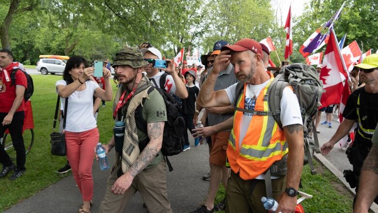 A crowd of people walks beside a man in an orange vest, with some taking his photo.