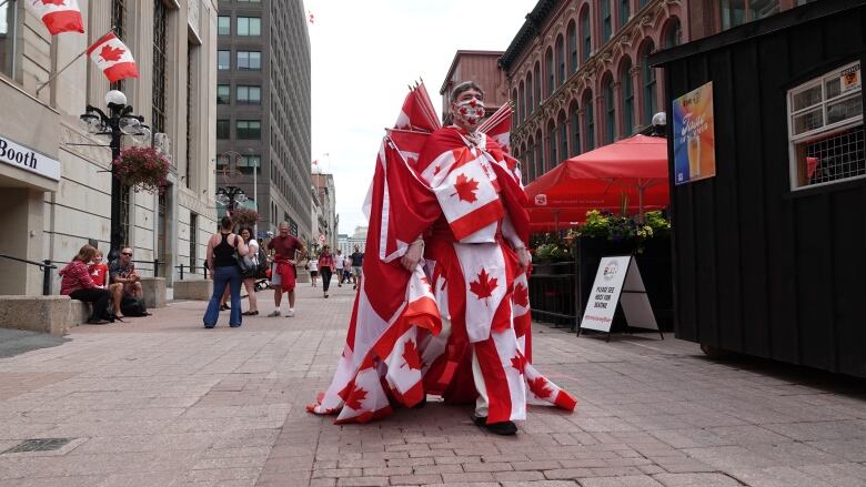 A man walks down a street while covered in Canadian flags.