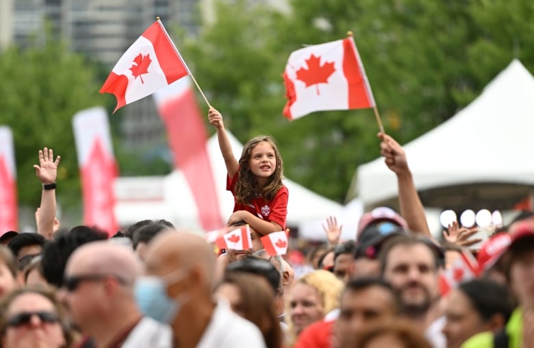 A child waves a Canadian flag while being lifted above a crowd of people.