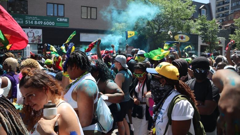 A crowd of Montrealers, many of them from the West-Indies, attend a parade along Saint-Catherine Street. Country flags can be seen being waved throughout the crowd. 