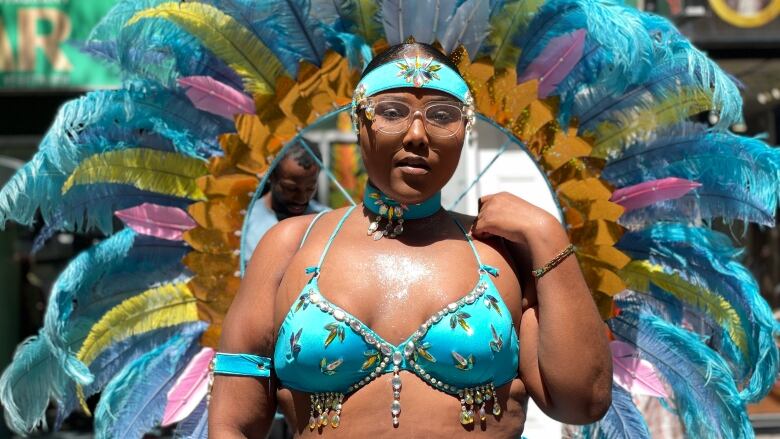 An attendee poses showing off an impressive blue caribana costume, with a circle of feathers behind her back. 