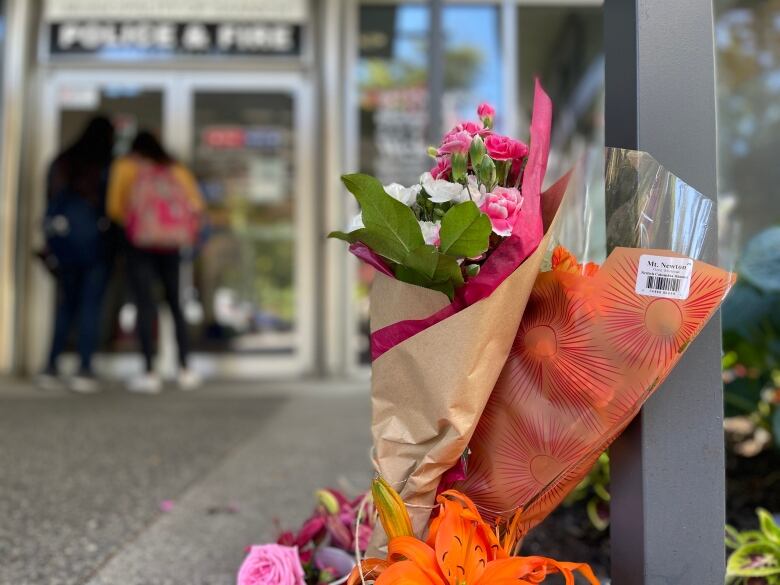 Members of the public look through the doors of Saanich, B.C.'s police department on Thursday, June 30, 2022, where bouquets of flowers have been placed in support of wounded officers  two days after a bank robbery ended with six officers wounded, two suspects dead, and locals reeling from the traumatic events.