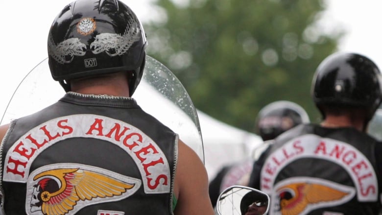 The backs of two Hells Angels are seen. They are both wearing helmets and leather vests with Hells Angels patches on them.