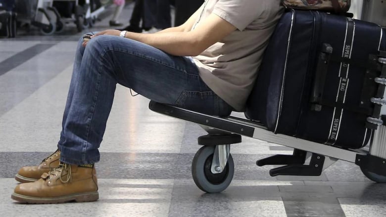 A person sits on a baggage cart at an airport. 