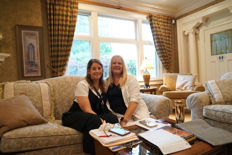 Two women sit on a sofa in a house.