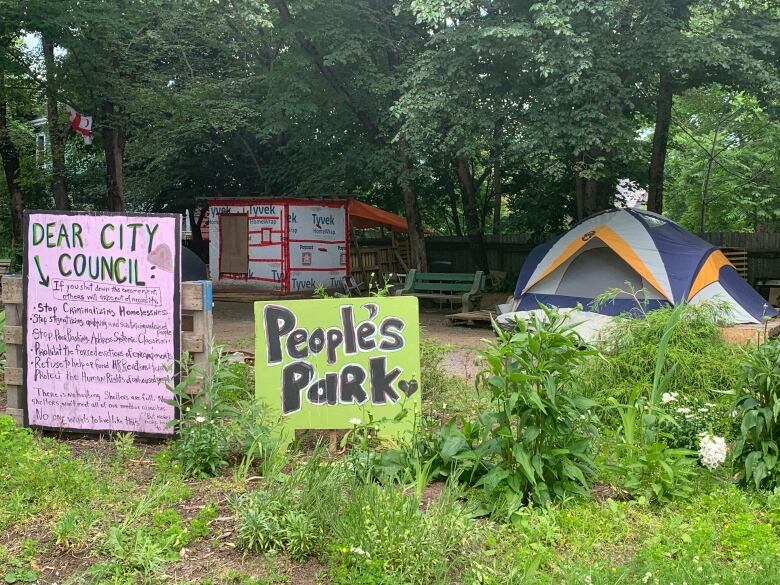 Image of tents and small structures in Meagher Park behind a signs that read 