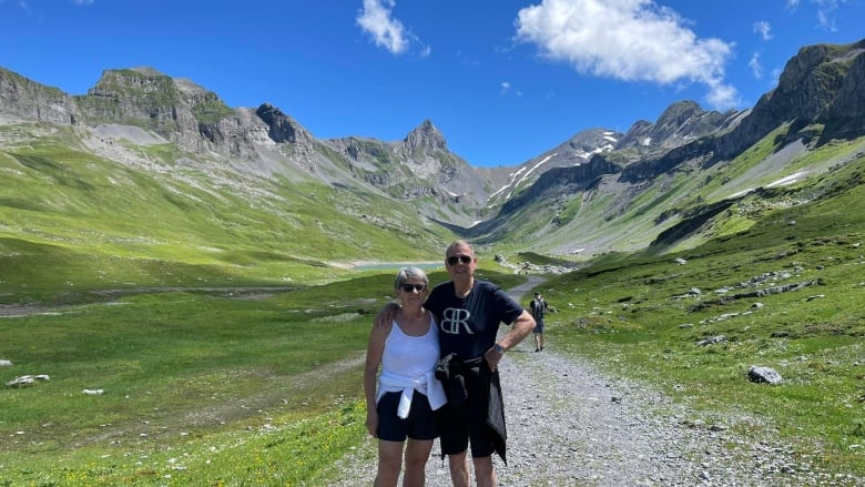 A couple stand next to each other with mountains in the background.