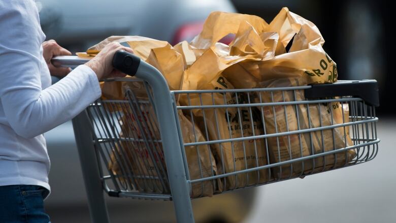 A woman pushes a shopping cart full of plastic grocery bags.