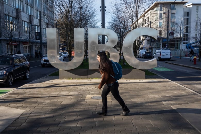 student with a backpack walks past large UBC letters