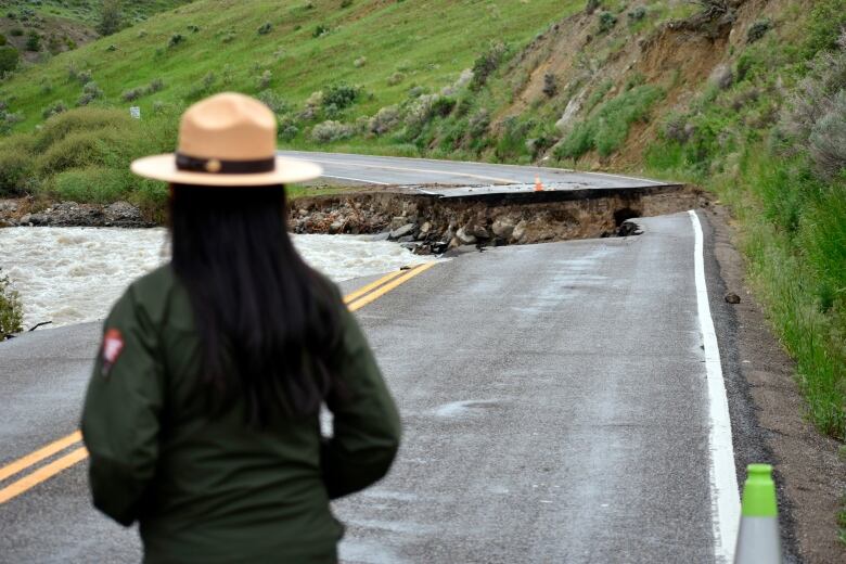 A photo shows the back of a park ranger, looking out at a washed out road damaged in the floods near Gardiner, Montana.